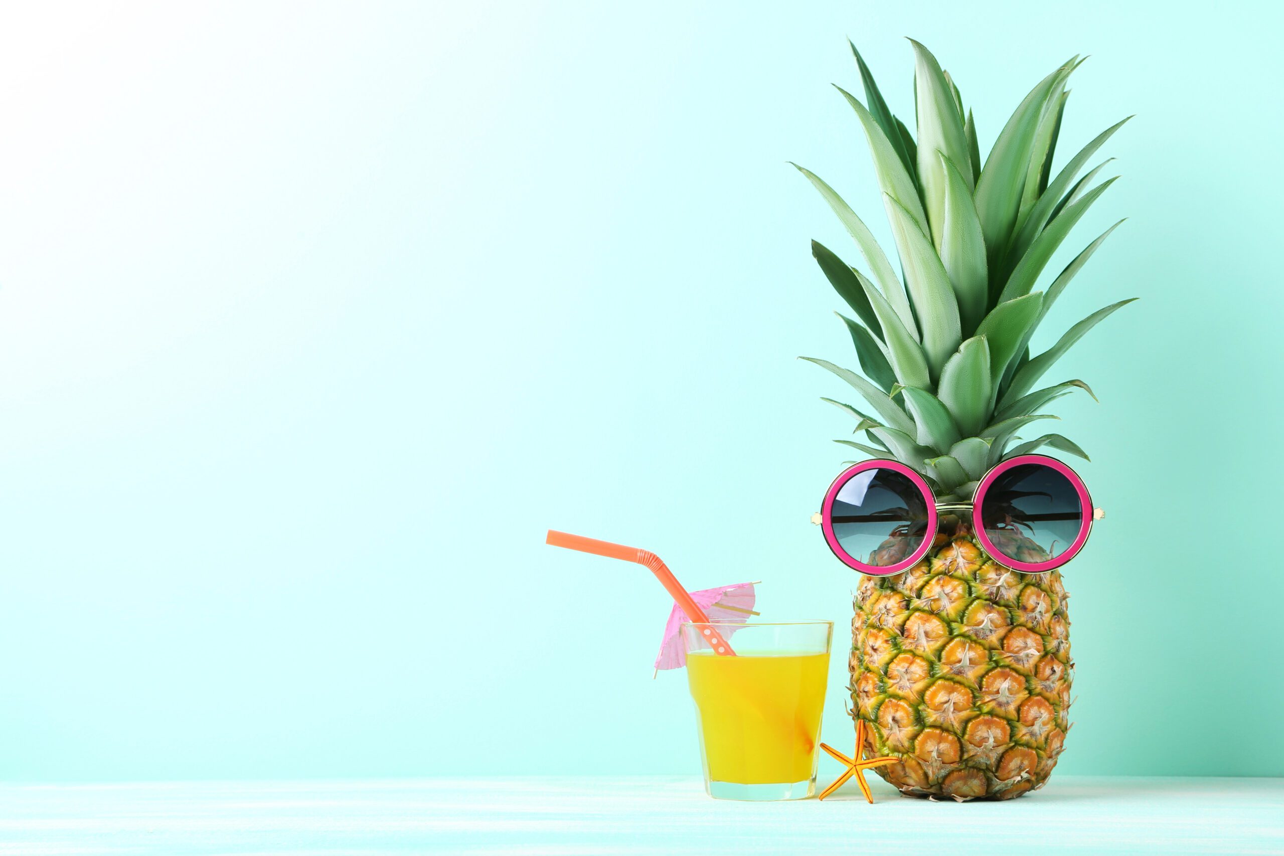 Ripe pineapple with sunglasses and glass of juice on mint background